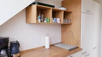 Eine Küchenzeile mit einer Kaffeemaschine, einem Papiertuchspender und einem Regal mit Gläsern und Büchern.