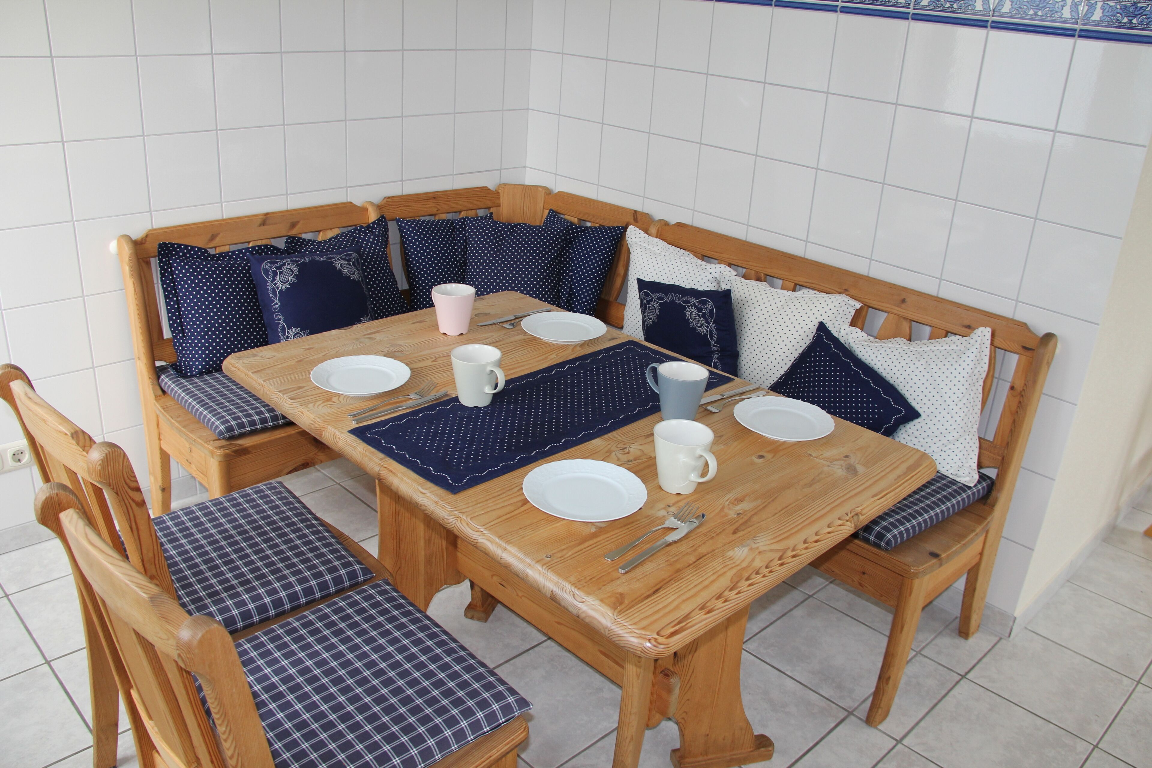 A wooden dining table with blue and white patterned cushions, white plates, and cutlery.