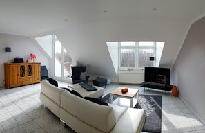 Ein geräumiges Wohnzimmer mit hoher Decke, einer Couch, einem Couchtisch, einem Fernseher und einem Kamin.