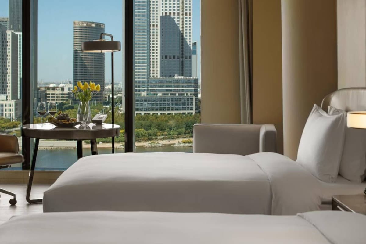Habitación de hotel con una cama grande, un escritorio con lámpara, una silla y vista a la ciudad.