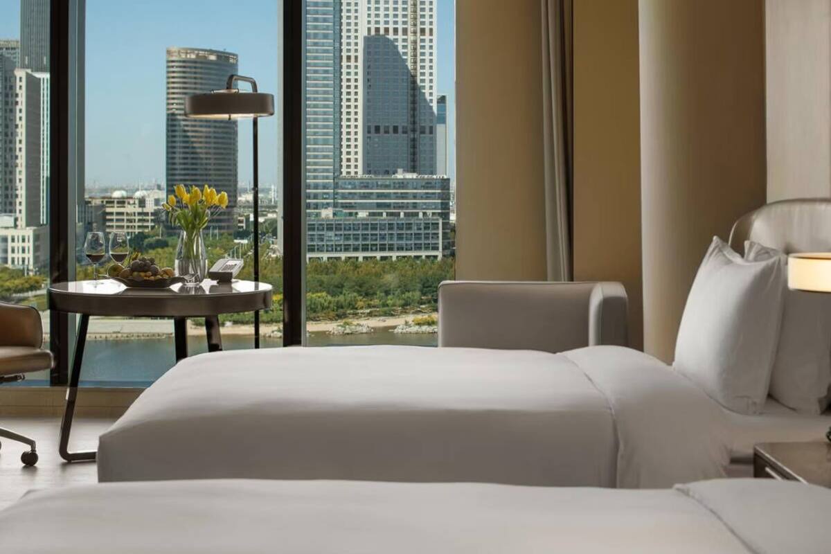 Habitación de hotel con una cama grande, un escritorio con lámpara, una silla y vista a la ciudad.