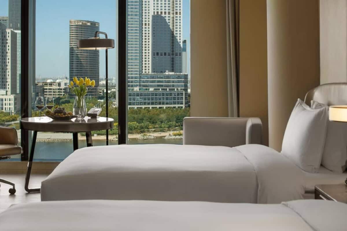 Habitación de hotel con una cama grande, un escritorio con lámpara, una silla y vista a la ciudad.