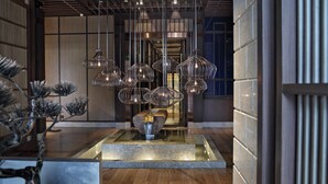 Een moderne lobby met een centraal waterkunstwerk, meerdere hanglampen en een houten vloer.