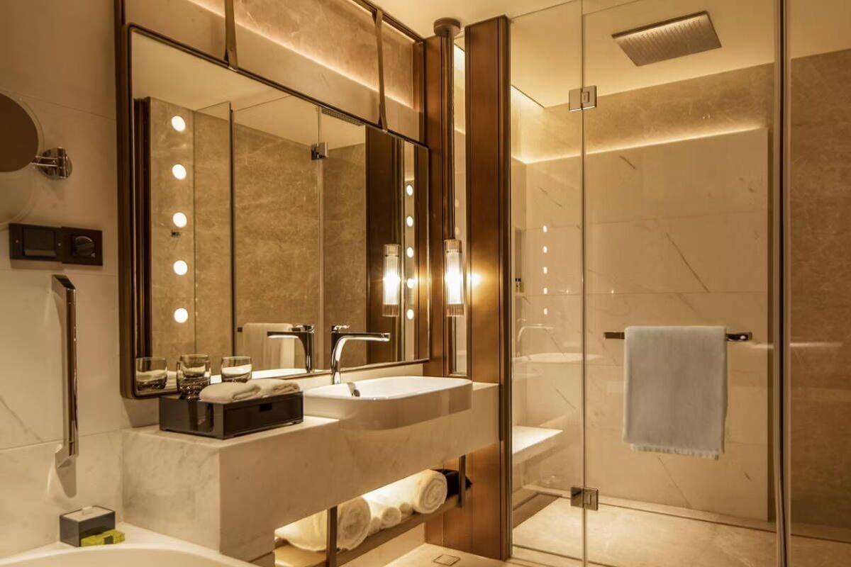 Un baño moderno con ducha envuelta en vidrio, tocador con dos lavamanos y un espejo grande con iluminación.