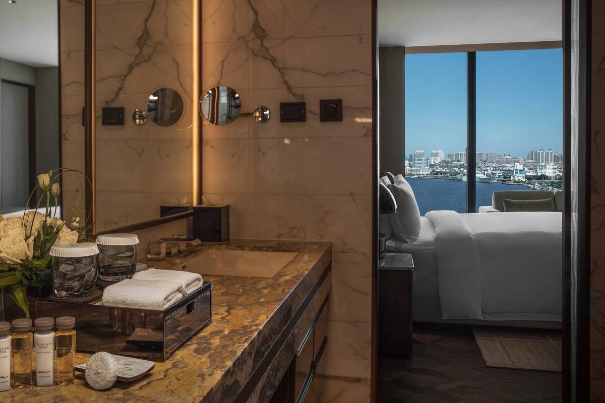 Un baño moderno con encimera de mármol, un espejo grande y vistas de la ciudad a través de un ventanal.