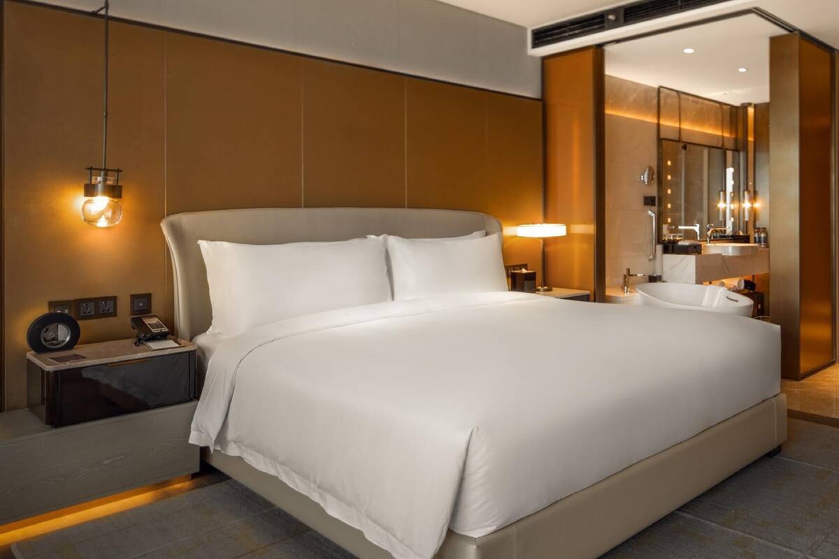 Una habitación de hotel moderna con una cama grande, lámparas de noche, un escritorio con teléfono y un baño con bañera y espejo.