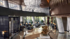 Een ruime lobby met een hoog plafond, modern meubilair en een centraal geplaatste sculptuur.