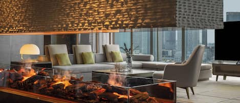 A modern living room with a glass-top fireplace, comfortable seating, and a city view.
