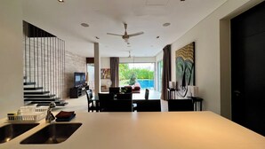 A modern kitchen with a central island, a dining area with a view, and a staircase leading to an upper level. - Baan Yamu By RESAVA (Pa Klok)