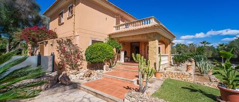 A two-story house with a stone facade, a balcony, and a well-maintained garden with cacti and shrubs.
