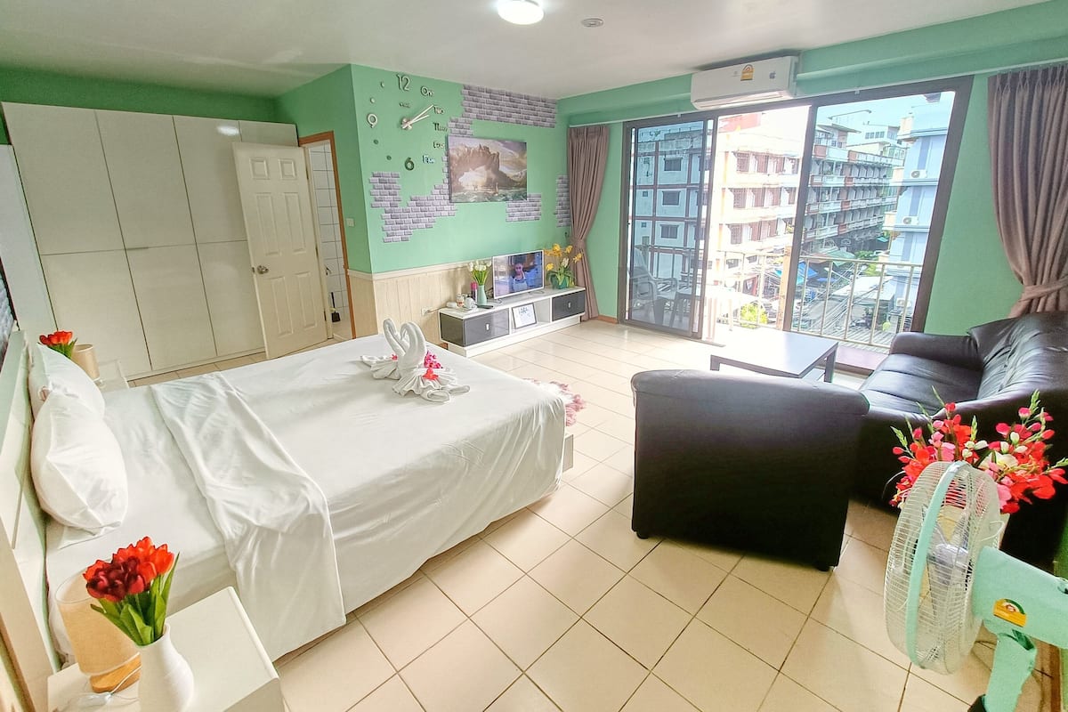 A hotel room with a bed, a sofa, a TV, and a balcony with a view of buildings.