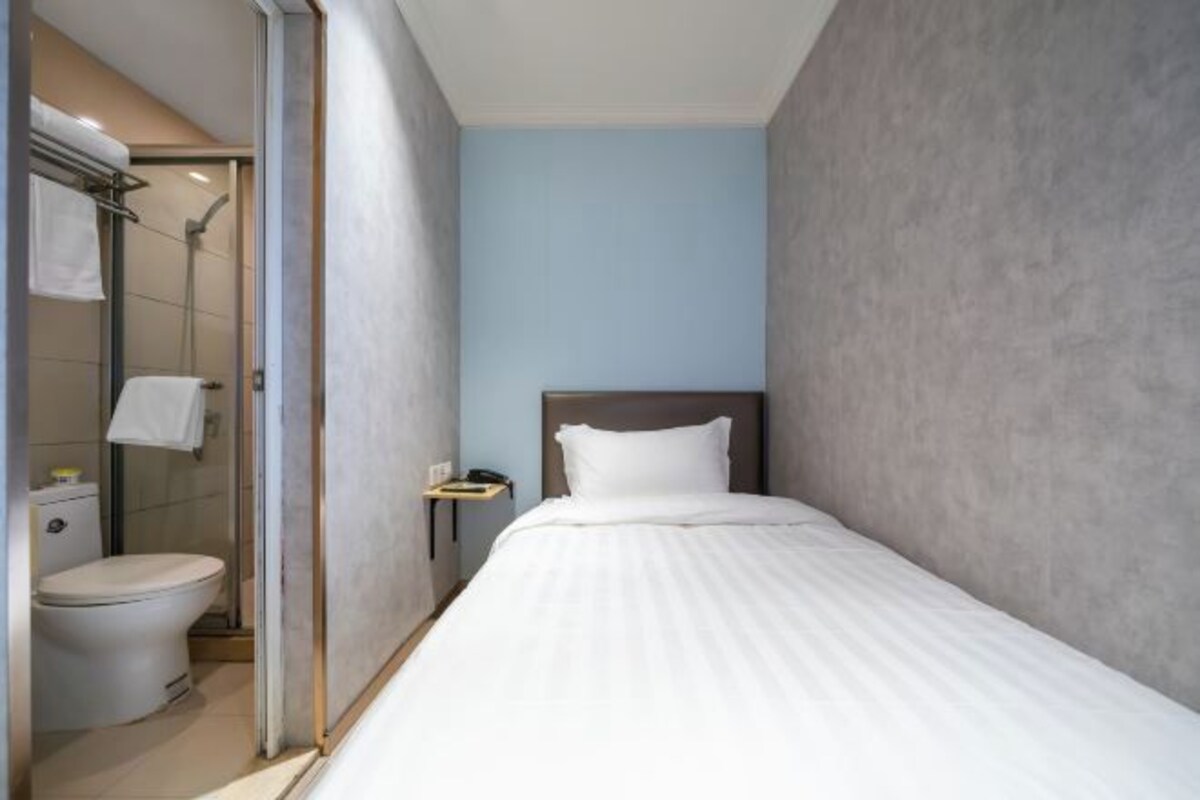Una habitación de hotel pequeña y moderna con una cama individual, una mesita de noche, ducha y un inodoro.