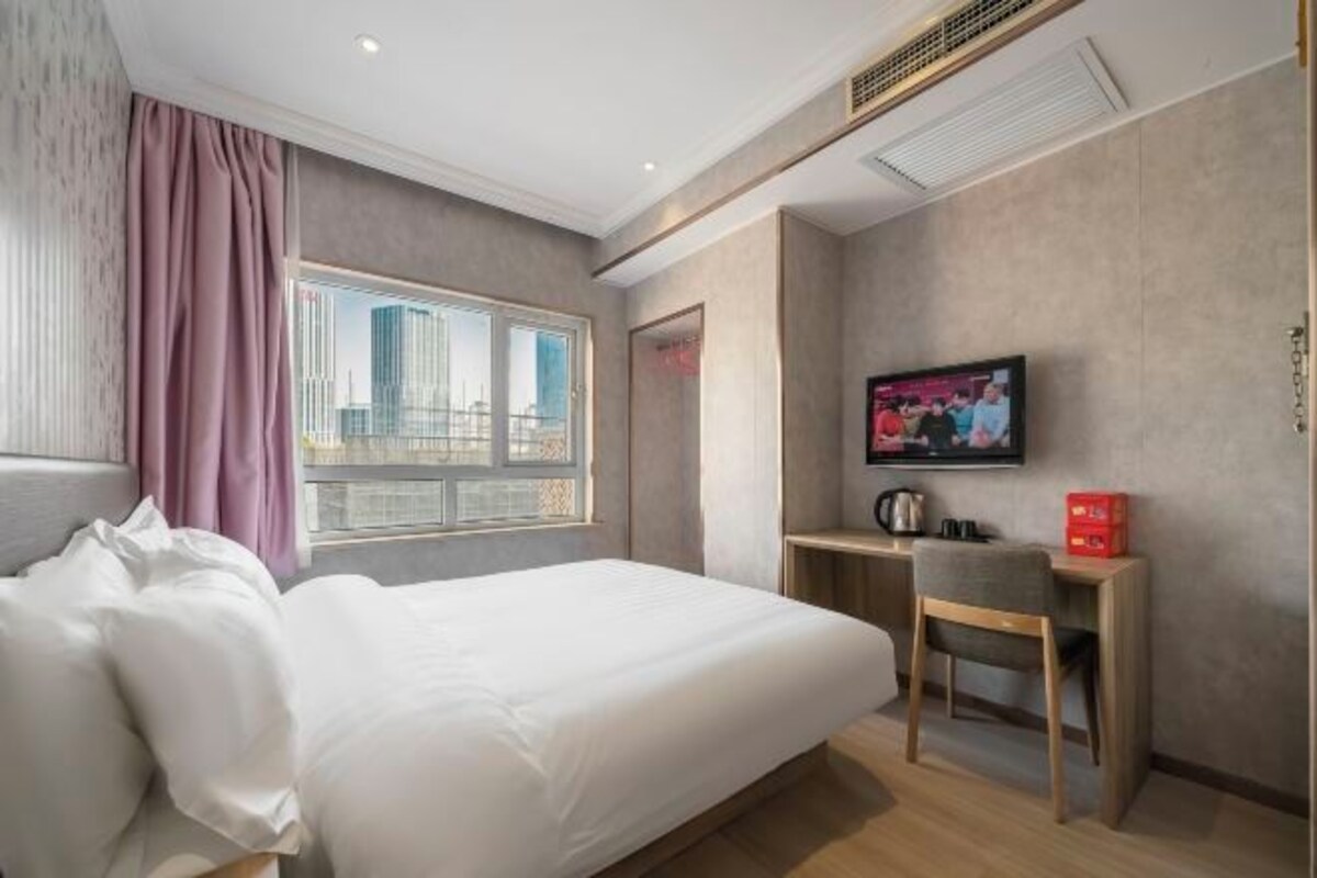 Habitación de hotel con cama, escritorio, televisor y ventana con vista a la ciudad.
