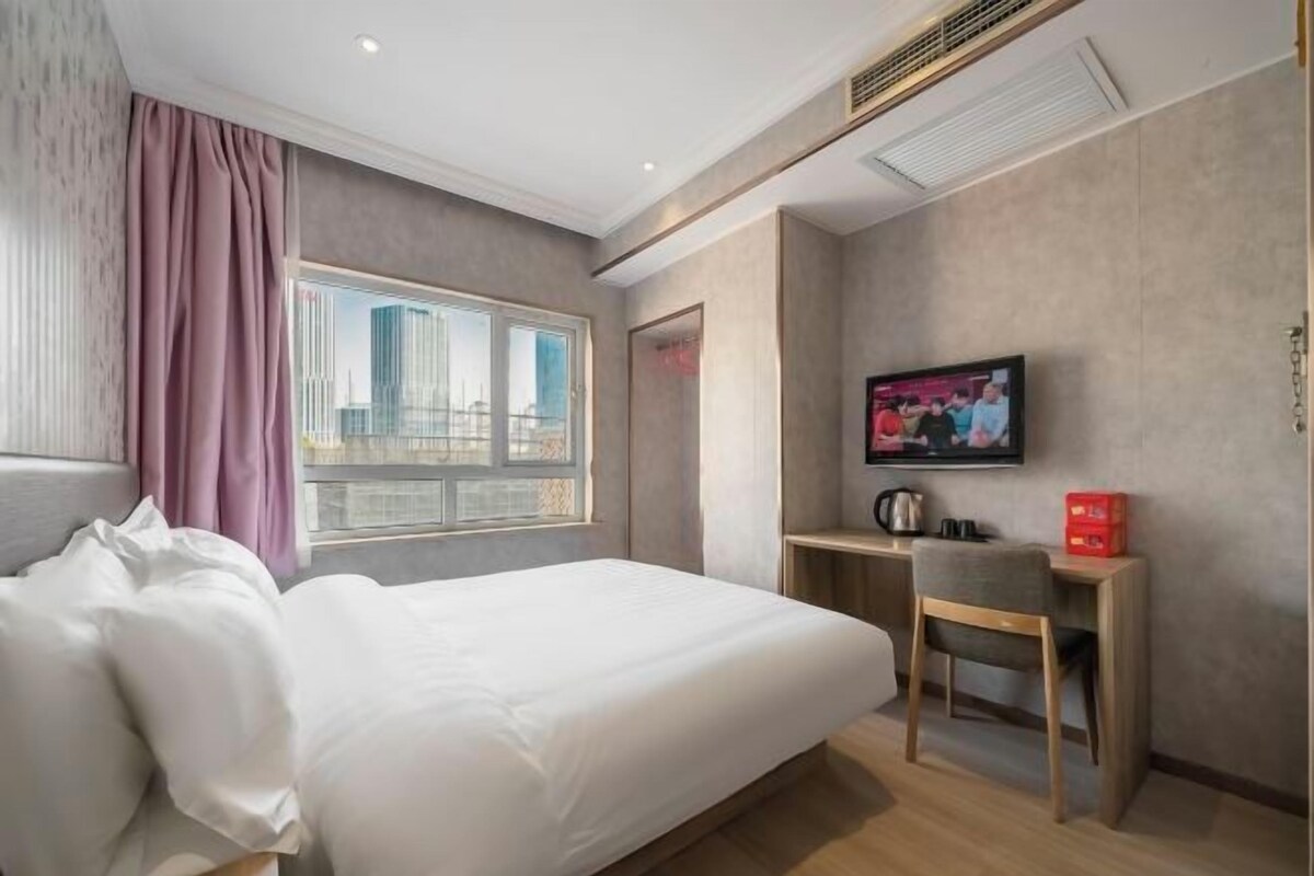 Ein Hotelzimmer mit Bett, Schreibtisch, Fernseher und einem Fenster mit Blick auf die Stadt.