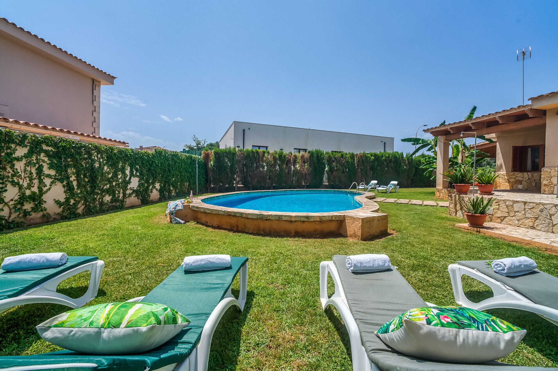 A backyard with a swimming pool, green lawn, and lounge chairs.
