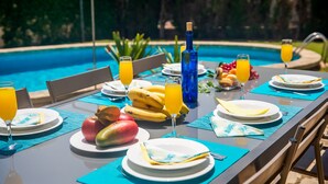 A dining table set with plates, glasses, and fruits by a pool. - Finca Rosas 28 with private pool in Mallorca (Manacor)