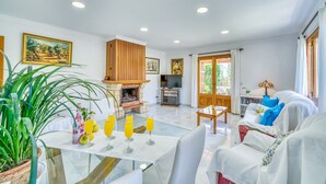 A spacious living room with a fireplace, a television, and a dining area with a table set for four. - Finca Rosas 28 with private pool in Mallorca (Manacor)
