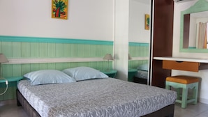 Ein Bett mit einem gemusterten Überwurf, ein Nachttisch mit einer Lampe, ein kleiner Hocker und ein Spiegel an der Wand.