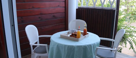 A small round table with a light green tablecloth, two white chairs, and a tray with breakfast items.