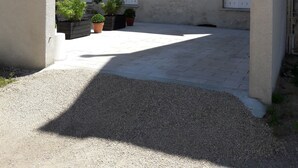 A courtyard with a gravel path, potted plants, and a building with a white door and window. - Cottage with terrace and parking. (Blois)