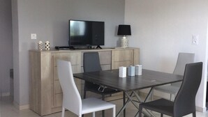 A modern dining area with a dark wooden table, four chairs, a television, and a lamp on a wooden cabinet. - Studio, two people, Haut-Doubs, Plateau du Pays Horloger between Maîche and Mor (Le Russey)