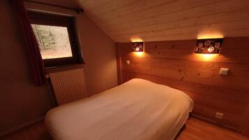 A bedroom with a bed, wooden walls, a window with curtains, and wall-mounted lights.