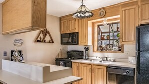 A modern kitchen with wooden cabinets, a black refrigerator, a microwave, a stove, and a dishwasher.