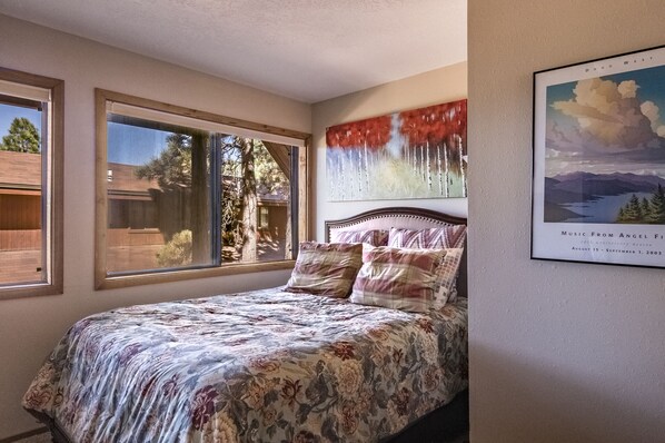 A bedroom with a large bed, two windows, a painting, and a framed picture on the wall. - Make your reservation now for a fun time in the mountains! (Angel Fire)