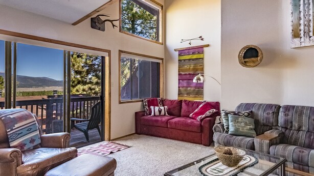 A spacious living room with large windows, a red sofa, a striped couch, and a glass coffee table.