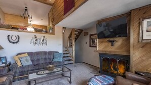 A cozy living room with a fireplace, a sofa, a coffee table, and a staircase leading to another level.