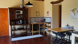 Une cuisine compacte avec des meubles en bois, un four à micro-ondes et un petit réfrigérateur. On y trouve une table à manger en bois, des tabourets de bar et un luminaire suspendu.