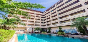 Un hôtel à plusieurs étages doté d’une piscine entourée de palmiers et de chaises longues.