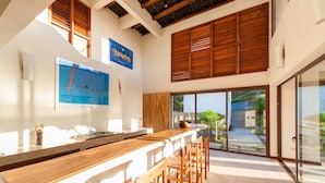 Una cocina moderna con barra de madera y taburetes, ventanas amplias y vistas al exterior.