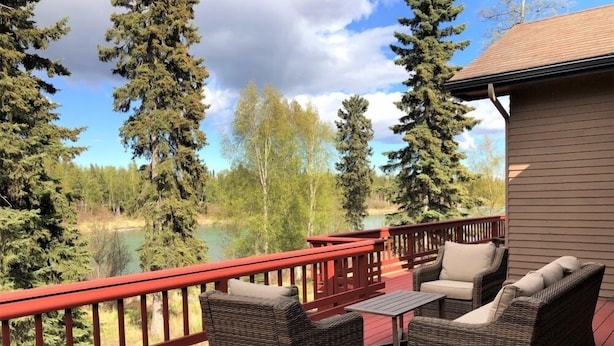 Une terrasse dotée de meubles en osier et offrant une vue sur un lac entouré d’arbres.