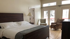 Une chambre à coucher avec un lit en bois, une chaise, une lampe et une vue sur l’extérieur par une porte.
