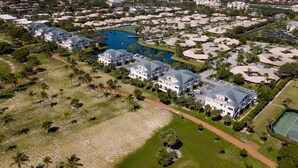 Vista aérea de una zona residencial con varias casas, una gran masa de agua y una cancha de tenis.