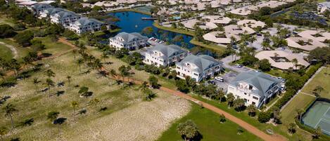 An aerial view of a residential area with multiple houses, a large body of water, and a tennis court.