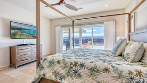 A bedroom with a large bed, a ceiling fan, a TV on a wooden dresser, and a balcony with a view of the city. - 3 Bedroom Home with a Pool at Waikoloa Beach Resort (Waikoloa)