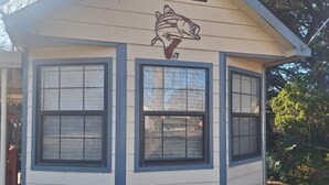 A small, single-story building with a peaked roof and a fish mural on the front. It has three windows and a small wooden bench outside. -  CLEAN, COZY LAKE CABIN COMFORT... (Clifton)