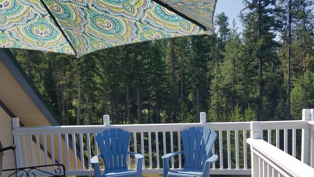 A wooden deck with two blue Adirondack chairs and a metal table, surrounded by a white railing. - Mountain retreat. (Marion)