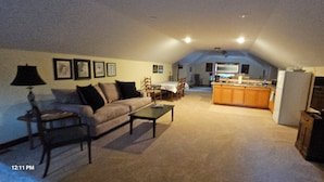 A living room with a sofa, coffee table, and lamp. There is a kitchen area with a refrigerator and stove. - Mountain retreat. (Marion)
