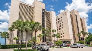 A modern hotel with multiple high-rise buildings, palm trees, and a parking lot with several cars.