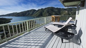 A deck with two lounge chairs and a small table, overlooking a bay with boats and green hills in the background. - Million Dollar Panoramic Views! Huge Decks and  Pool! (Coral Bay)