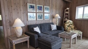 A cozy room with a dark grey sofa, a floral armchair, and a wooden ladder shelf. There are framed pictures on the wall and two table lamps on side tables. - Million Dollar Panoramic Views! Huge Decks and  Pool! (Coral Bay)