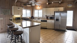 A modern kitchen with wooden walls, a central island, bar stools, and a stainless steel refrigerator. - Million Dollar Panoramic Views! Huge Decks and  Pool! (Coral Bay)