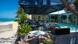 An outdoor seating area with tables and chairs, a pool, and a view of the ocean. - LUXURY PENTHOUSE!! Courtesy SUV Included, PaddleBoards, Bikes, Chairs & More! (Cockburn Town)