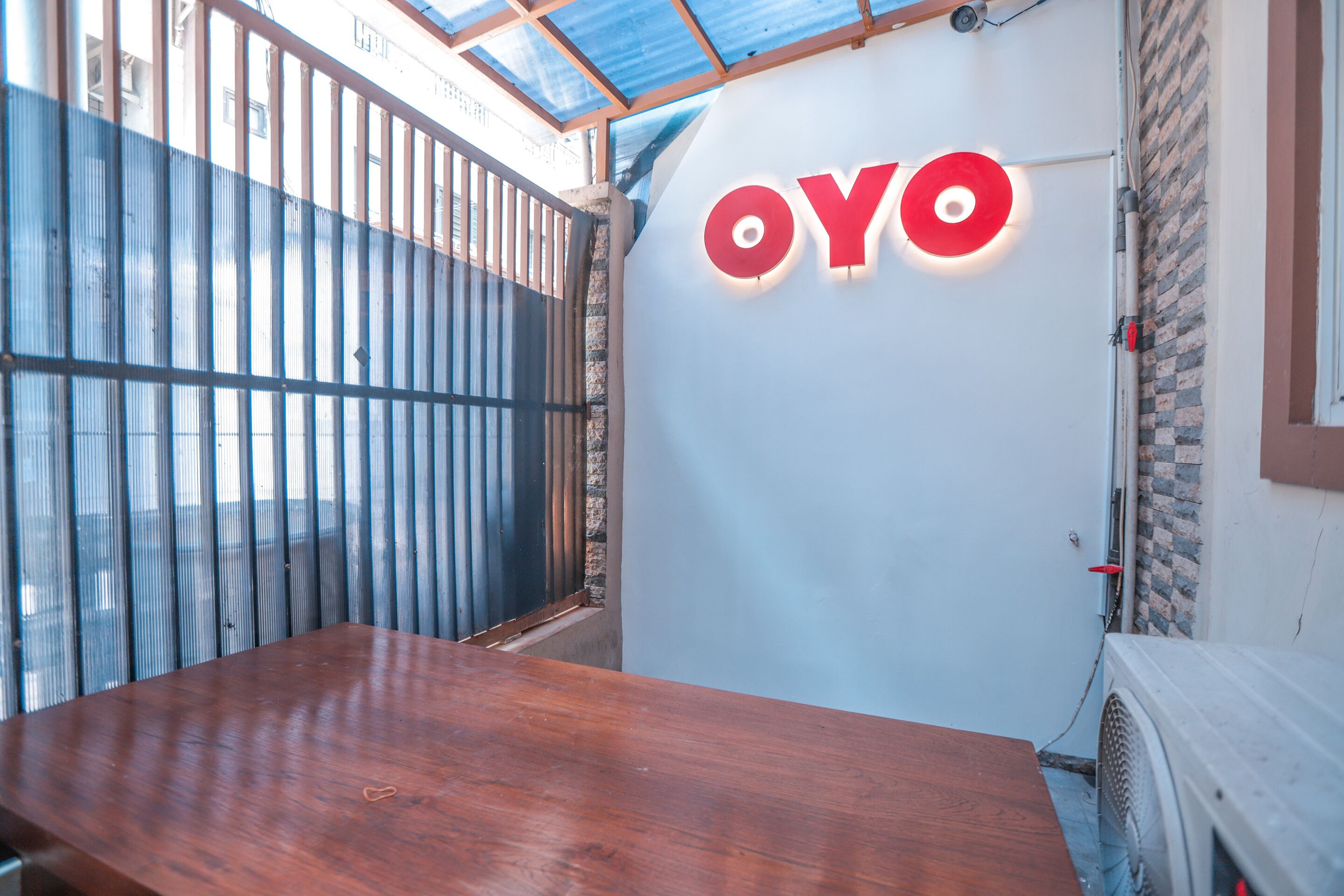 A room with a wooden table, a white wall with the 'OYO' logo, a metal gate, and a brick wall.