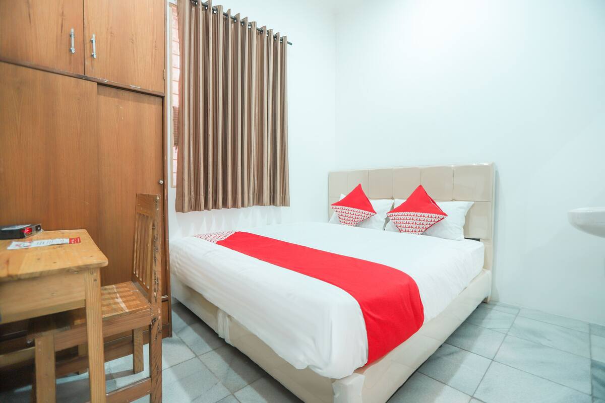 Un dormitorio ordenado con una cama, un armario de madera, una mesita y una silla.