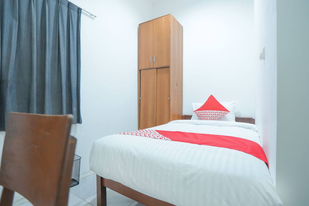 Un dormitorio con una cama, un armario de madera, una silla y una ventana con cortinas.