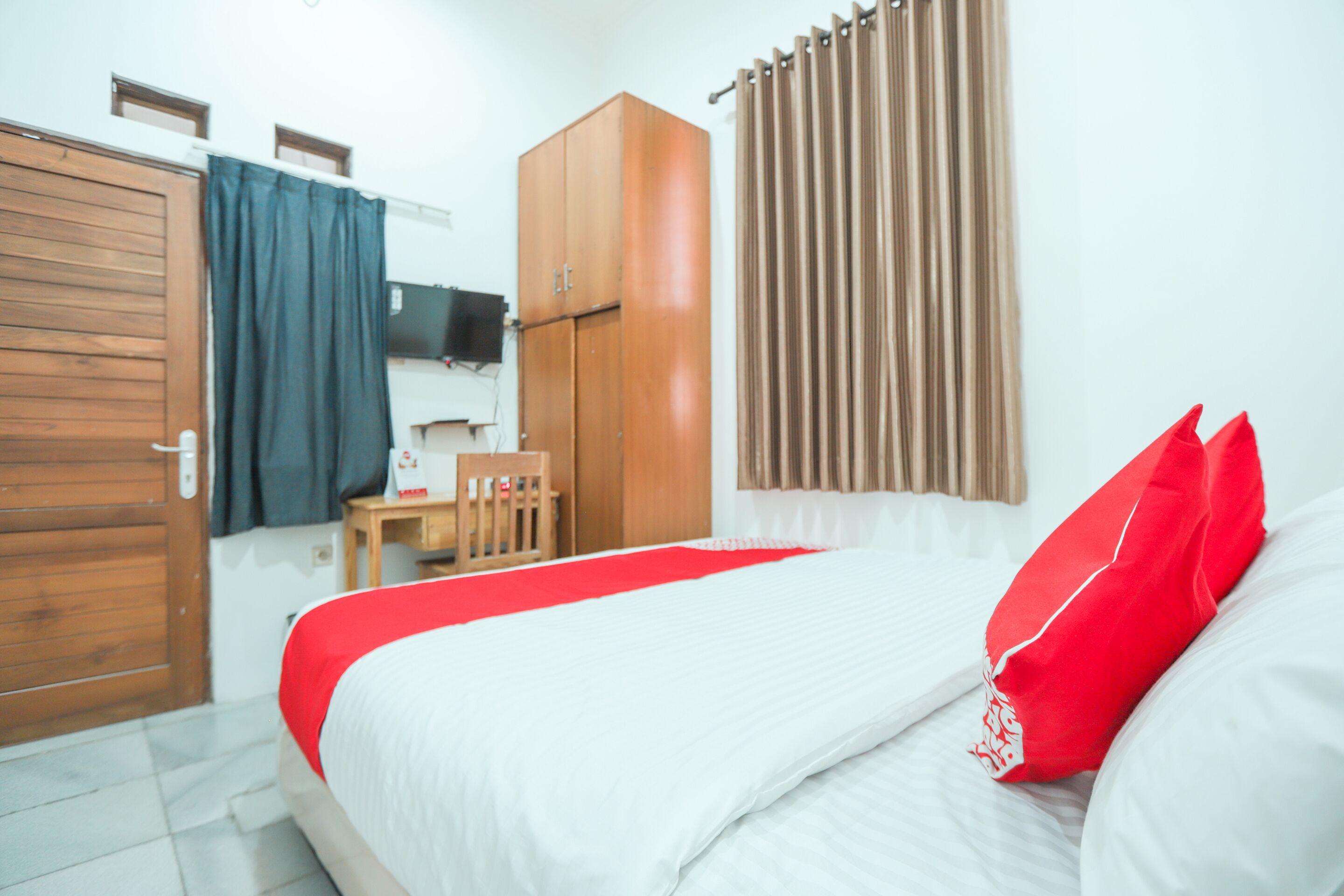 A hotel room with a bed, a wooden wardrobe, a desk, and a television.